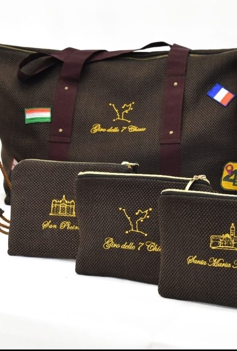 Il borsone e le pochette in tessuto marrone con il Giro delle 7 chiese ricamato in oro