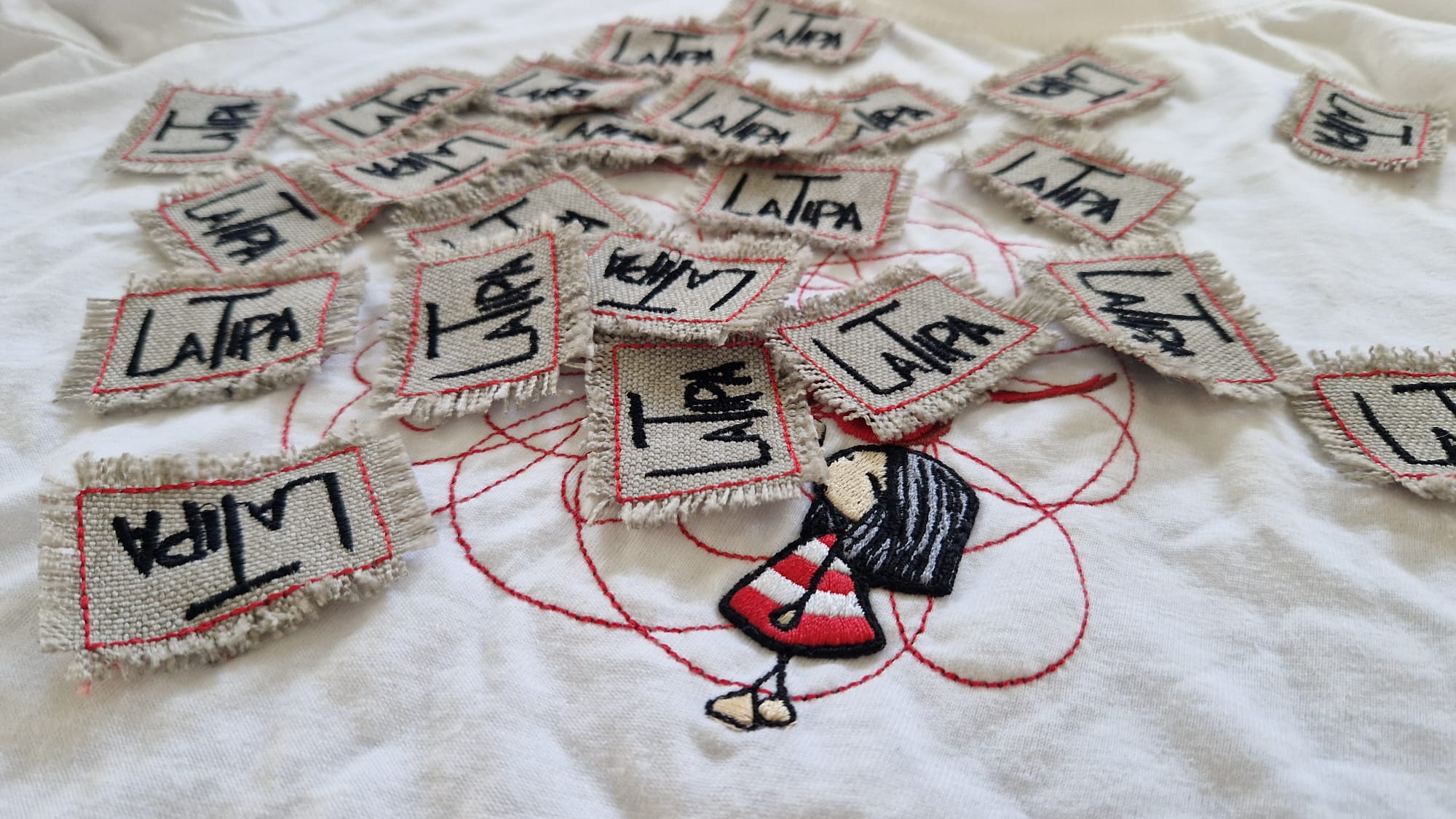 Etichette in tela con il logo La Tipa ricamato, sparse su una maglia con la Tipa ricamata
